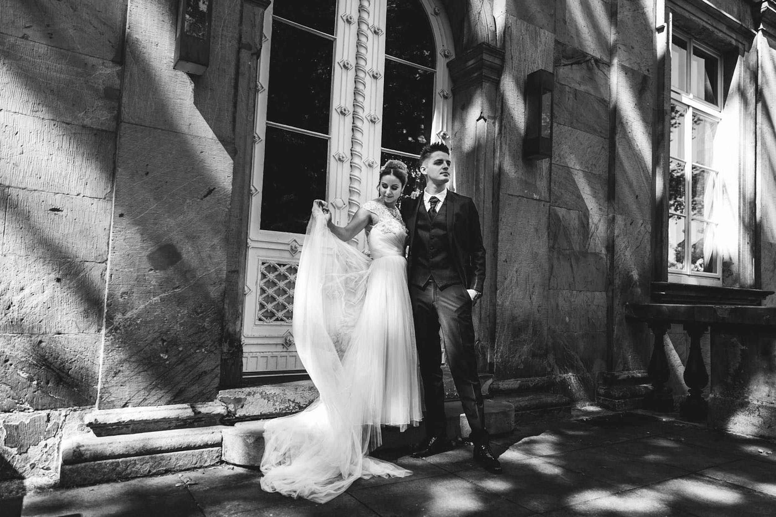 Fotoshooting am Hochzeitstag. Palaisgarten, Braut und Bräutigam stehen beieinander, die Braut spielt mit dem Schleier. Begleitung als Hochzeitsfotograf in Detmold.