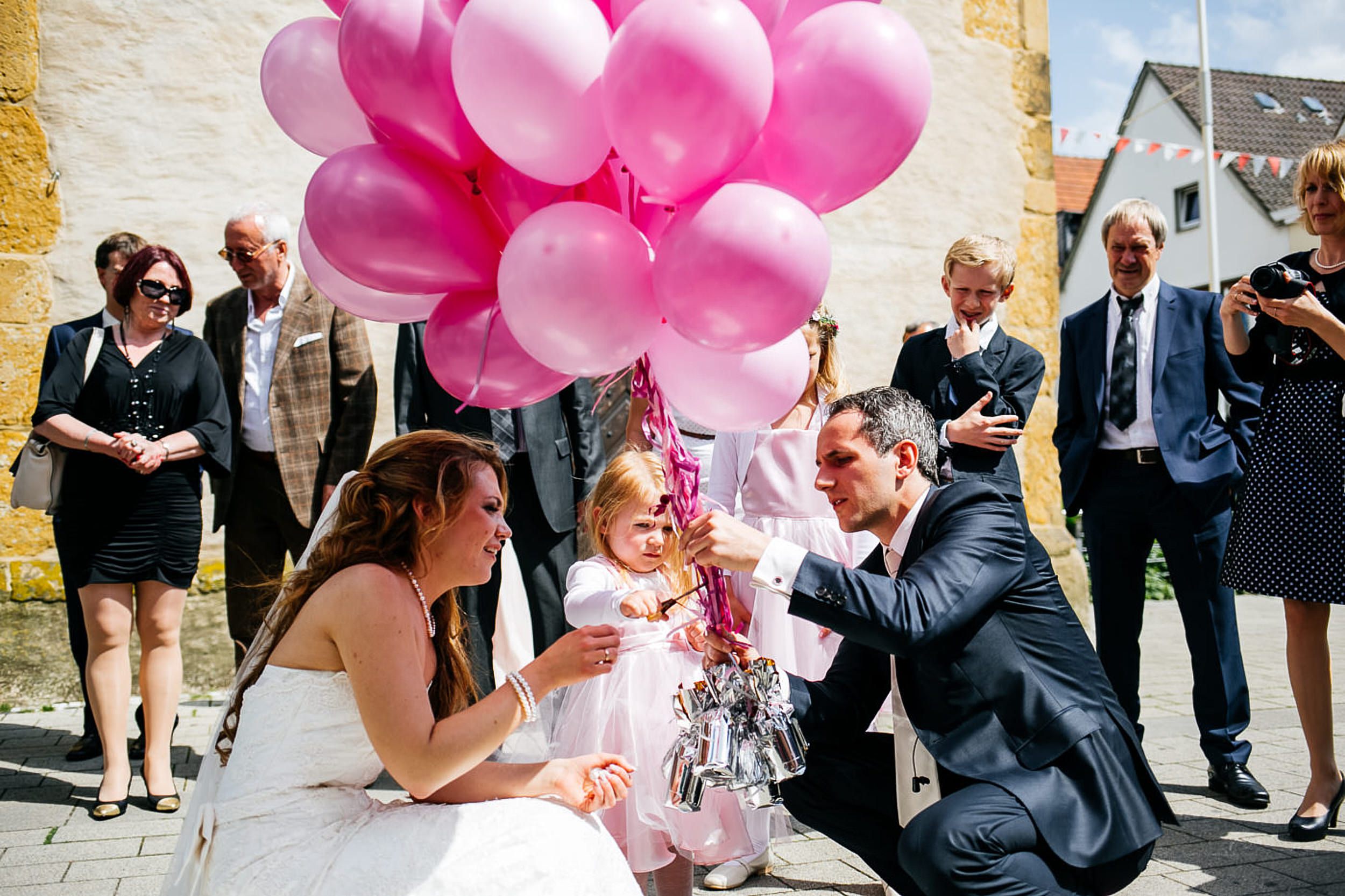 Hochzeitsfotograf fotografiert das Brautpaar mit den pinken Luftballons vor der Kirche.