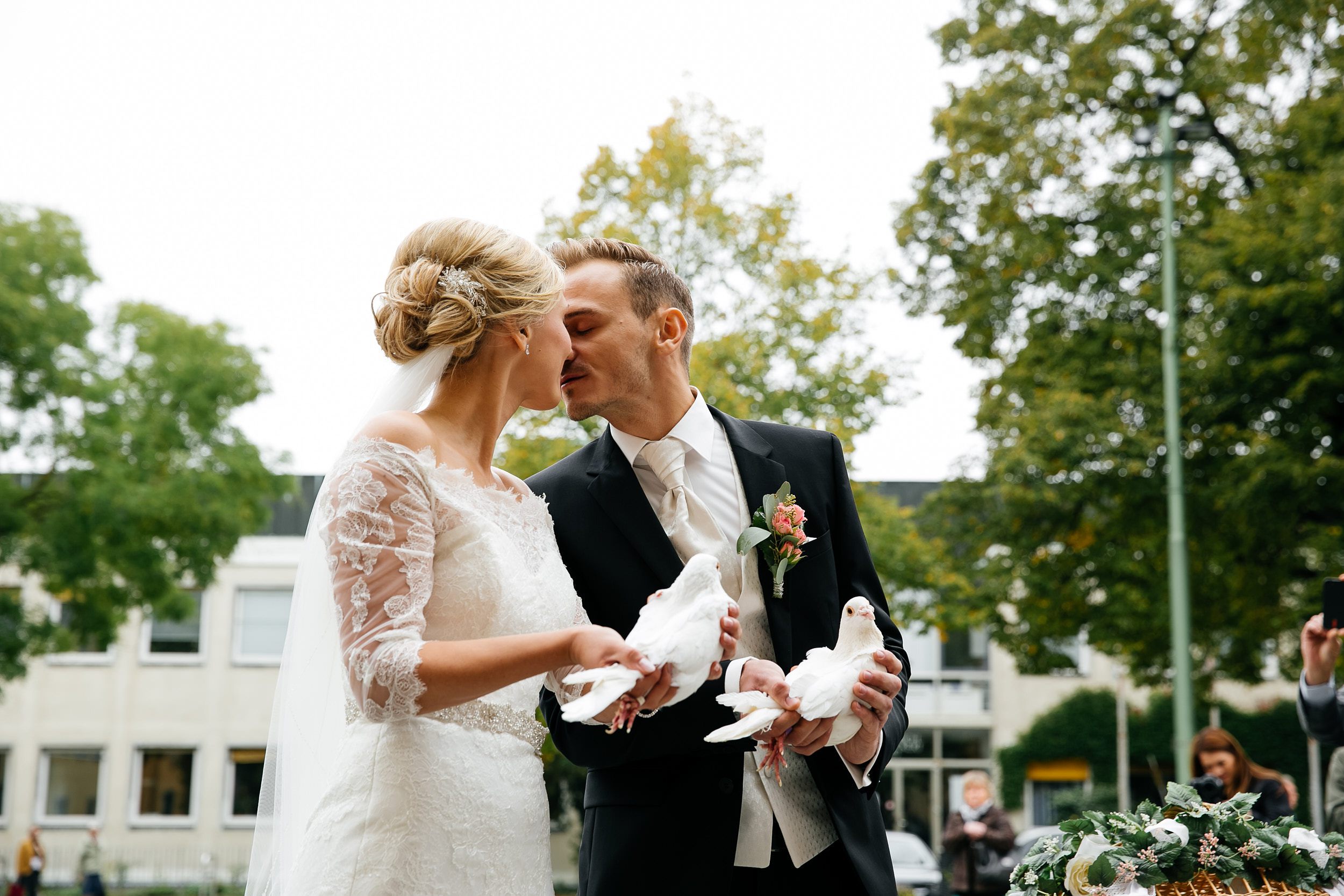 Kirchliche Trauung. Braut und Bräutigam halten die Tauben in den Händen und küssen sich. Hochzeitsfotograf in Schweinfurt.