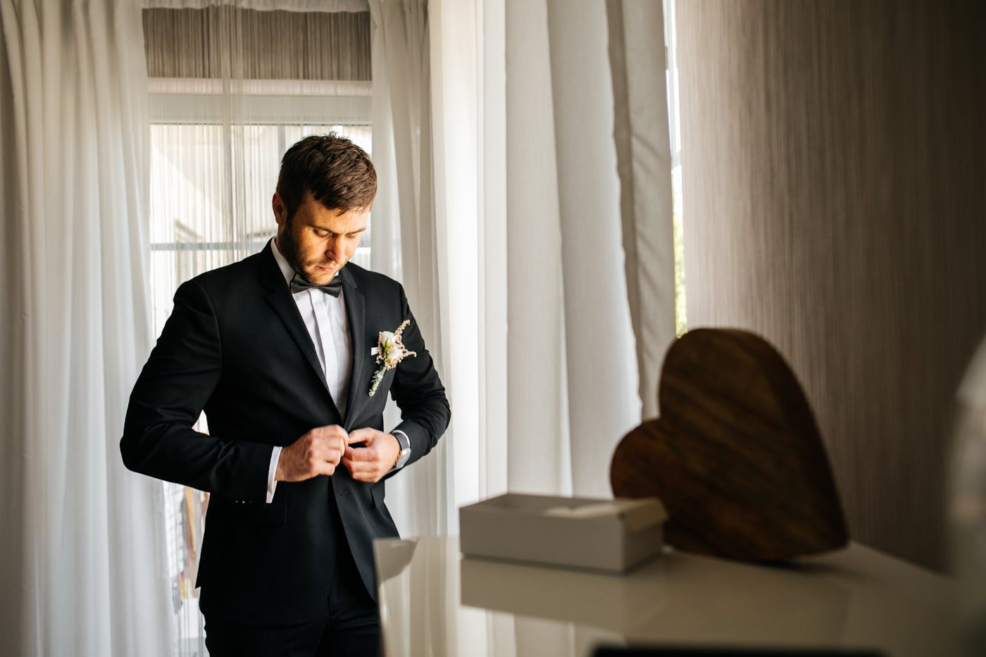 Bräutigam knöpft das Jacket am Fenster zu. Als Hochzeitsfotograf in Bad Ems.