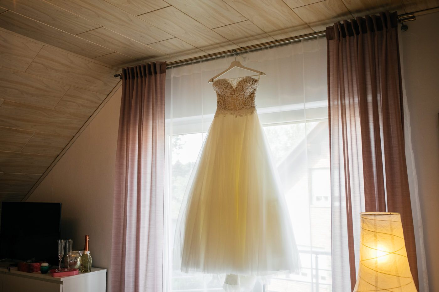 Brautkleid hängt am Fenster auf der Gardinen-Stange. Als Hochzeitsfotograf in Bad Ems.