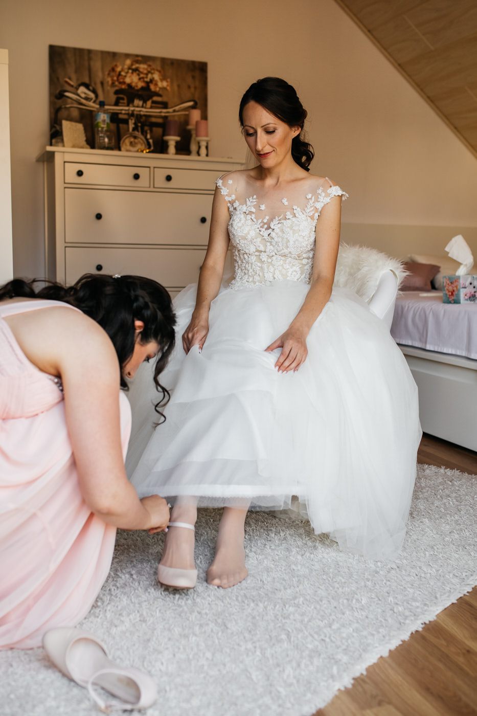 Vorbereitungen der Braut. Trauzeugin macht den Schuh der Braut zurecht. Als Hochzeitsfotograf in Bad Ems.