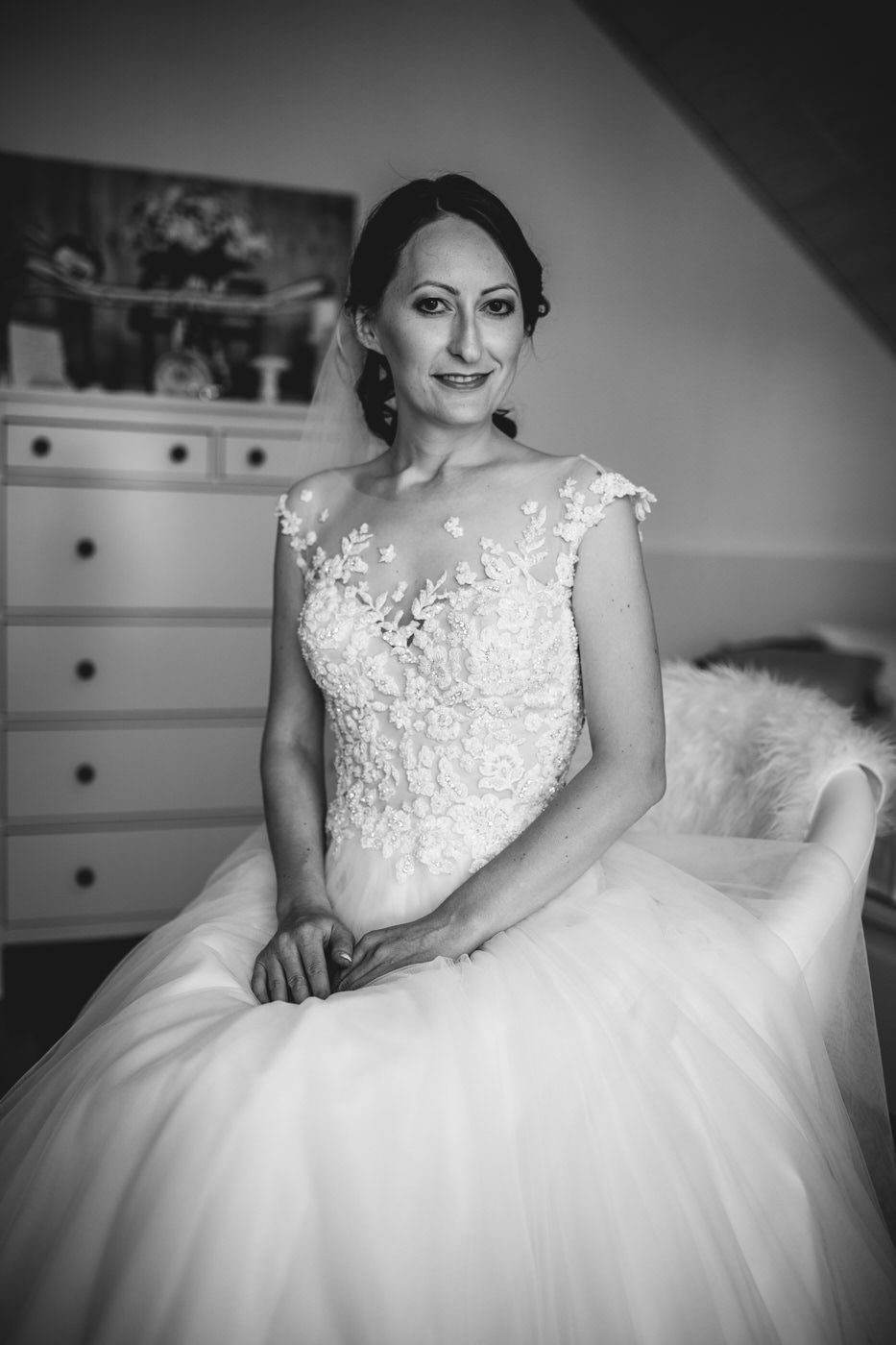 Vorbereitungen der Braut. Braut schaut in die Kamera sitzend auf dem Stuhl. Foto in schwarz weiß. Als Hochzeitsfotograf in Bad Ems.