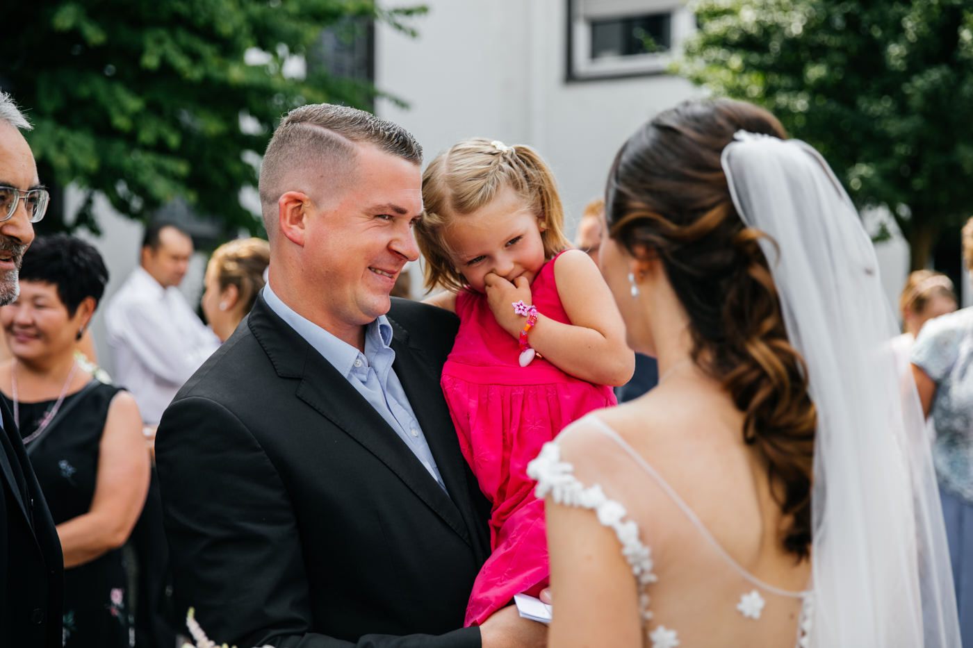 Kirchliche Trauung. Braut bei den Gästen. Kleins Mädchen im roten Kleid schaut verlegen zu der Braut. Hochzeitsfotograf in Bad Ems.