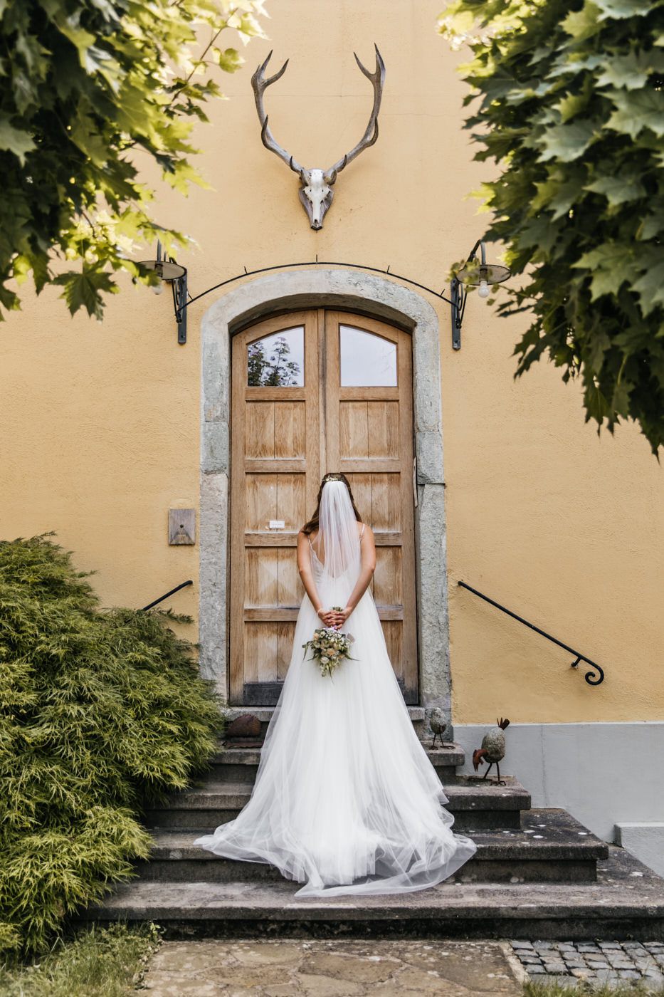 Fotoshooting am Hochzeitstag. Braun steht vor der Tür mit dem Braut Strauß hinterm Rücken.