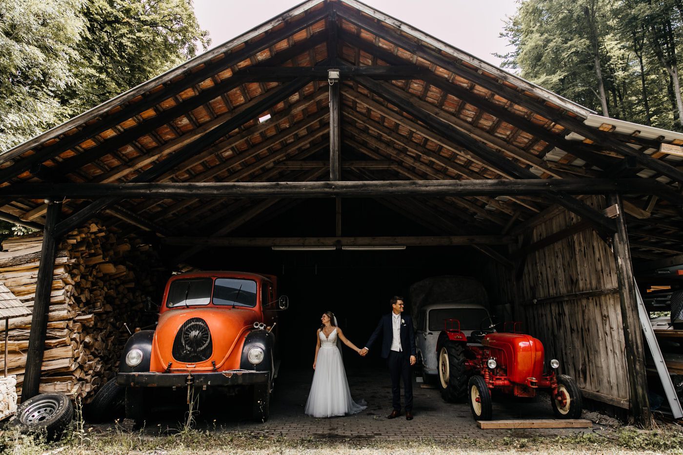 Hochzeitstag. Brautpaar-Shooting in der Scheune. Das Brautpaar steht in der Scheune zwischen zwei alten Traktoren.