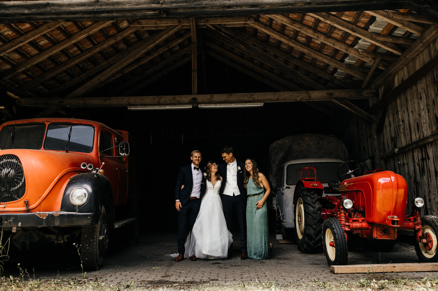 Fotoshooting in der Scheune. Brautpaar mit den Trauzeugen, umarmen sich und lachen.