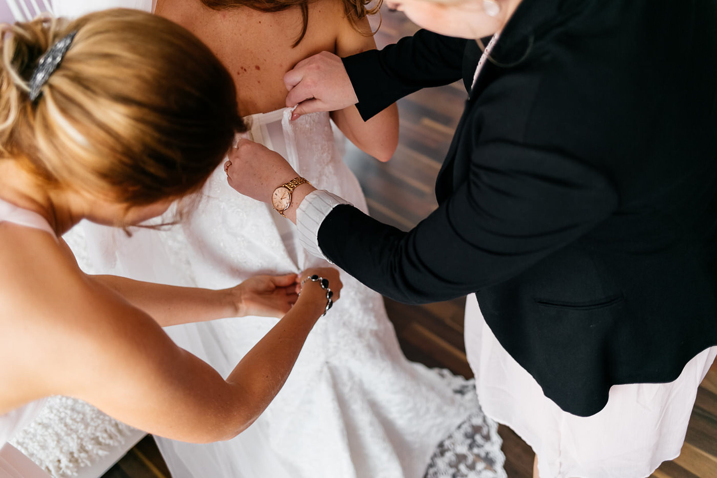 Brautjungfern machen das Brautkleid zu.