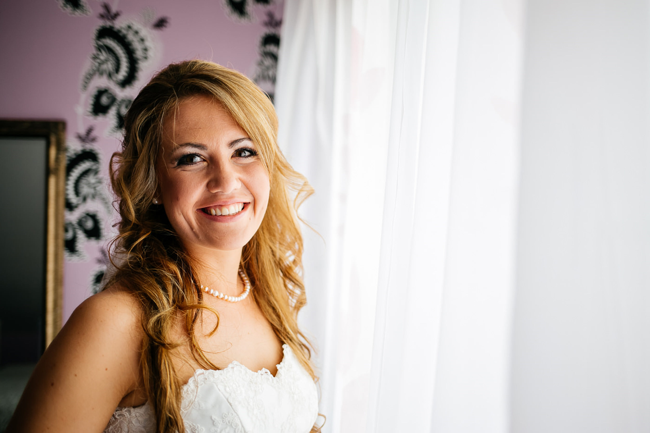 Braut steht vom Fenster, l&auml;chelt in die Kamera