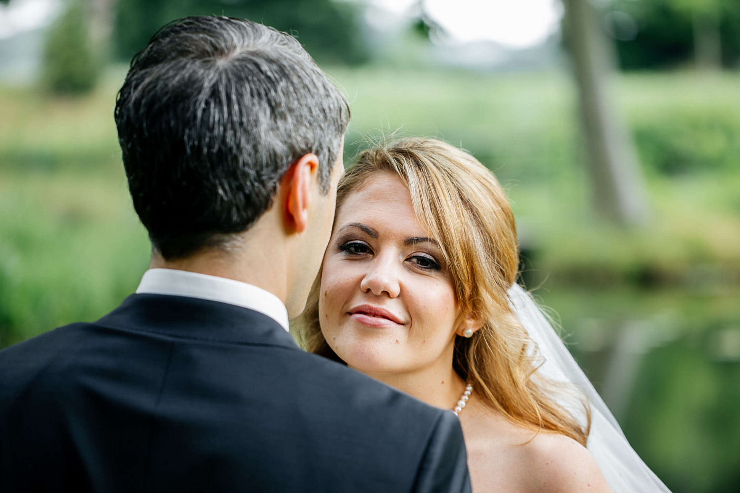 Braut schaut &uuml;ber die Schulter des Br&auml;utigam in die Kamera.