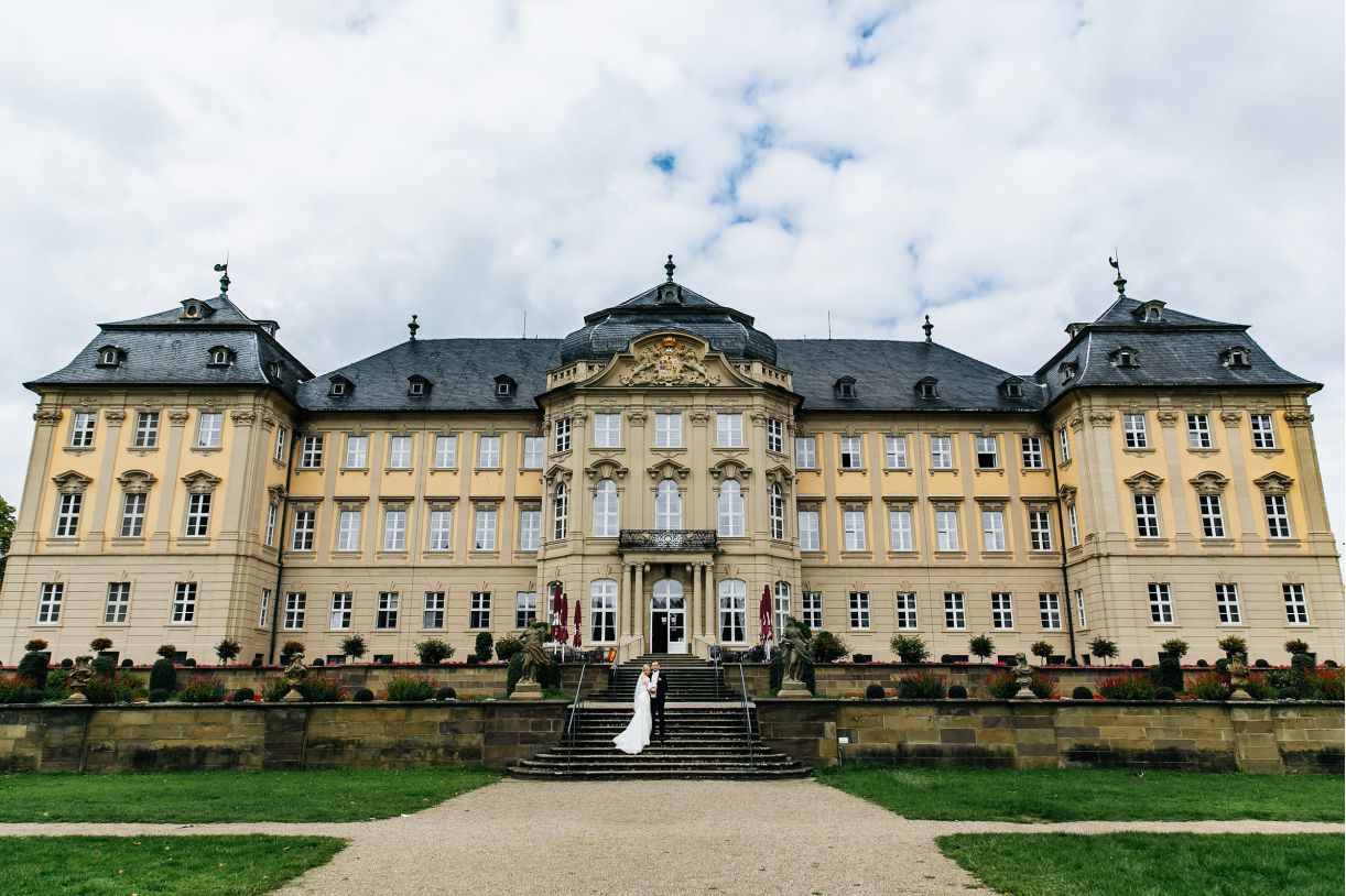 Das Brautpaar beim Fotoshooting. Braut und Bräutigam stehen vor dem Schloß. Hochzeitsfotograf in Schweinfurt.
