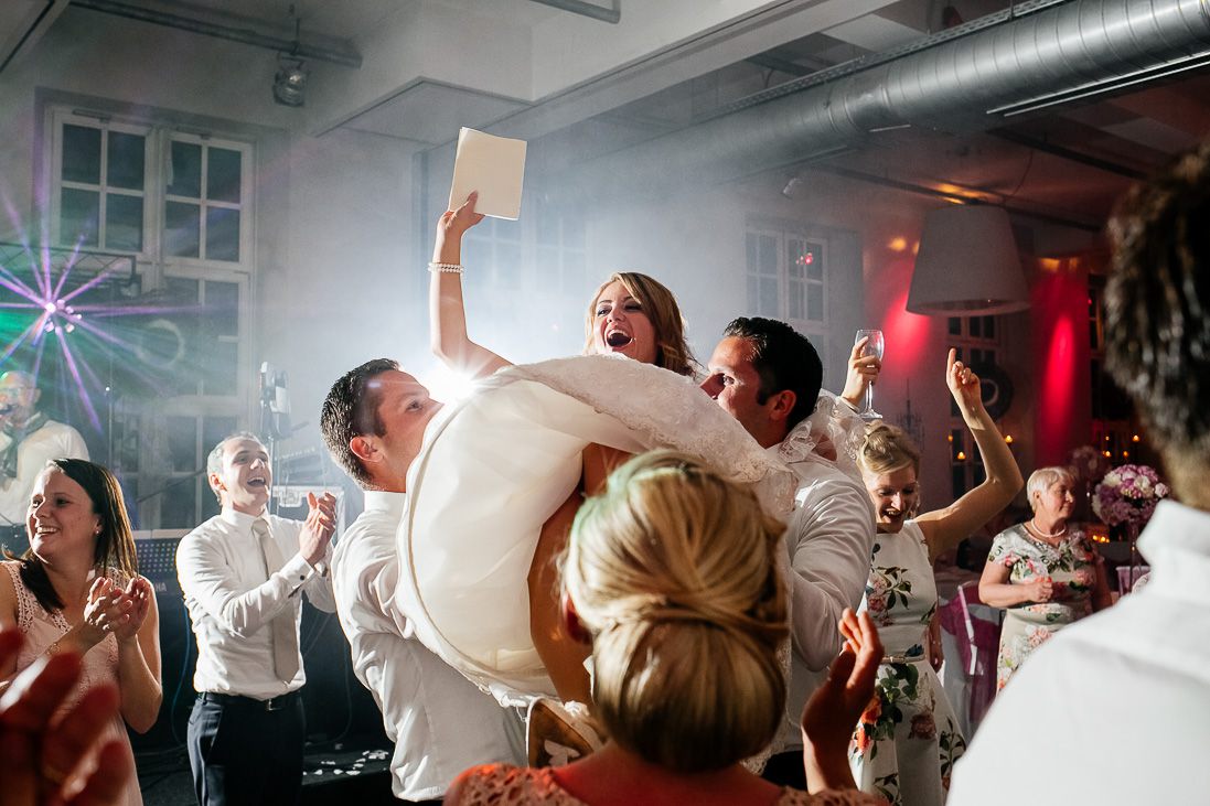Braut auf der Tanzfläche hochgehoben, umgeben von feiernden Gästen – Hochzeitsfotograf Münster